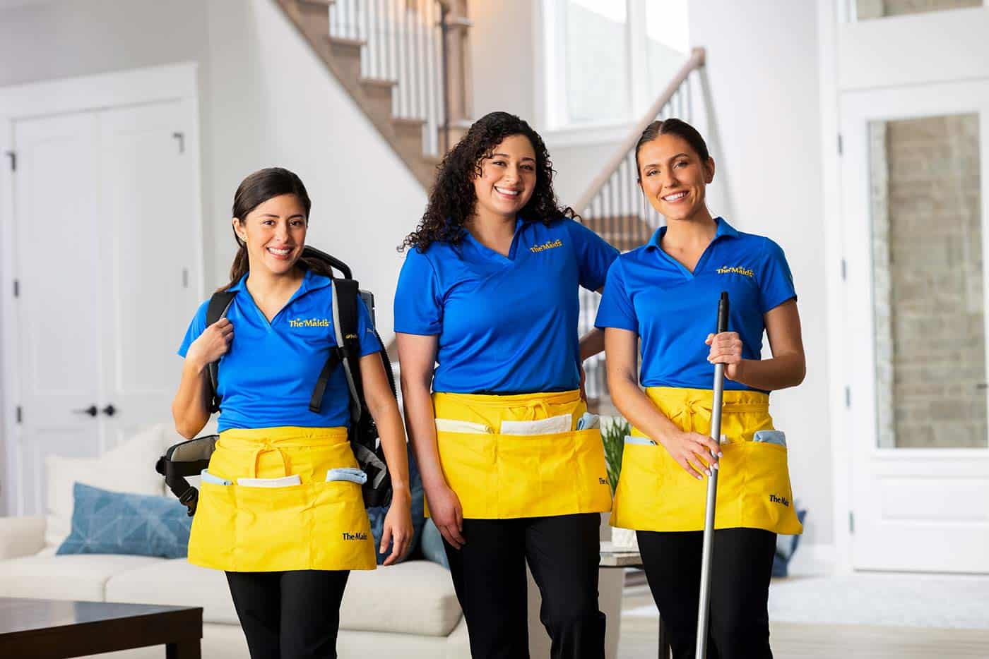 Three uniformed Maids of Scottsdale cleaners standing in a bright, modern living room ready to clean.